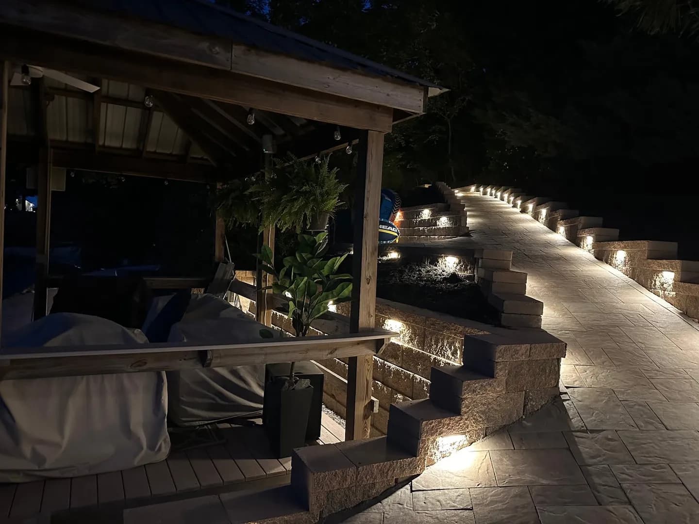 Night Lighting on Retaining Wall Steps by Alex's Lawnscape in Charlotte NC — Illuminated stone retaining wall steps with integrated LED landscape lighting, paver walkway, and covered patio area — shot at dusk to showcase the lighting design