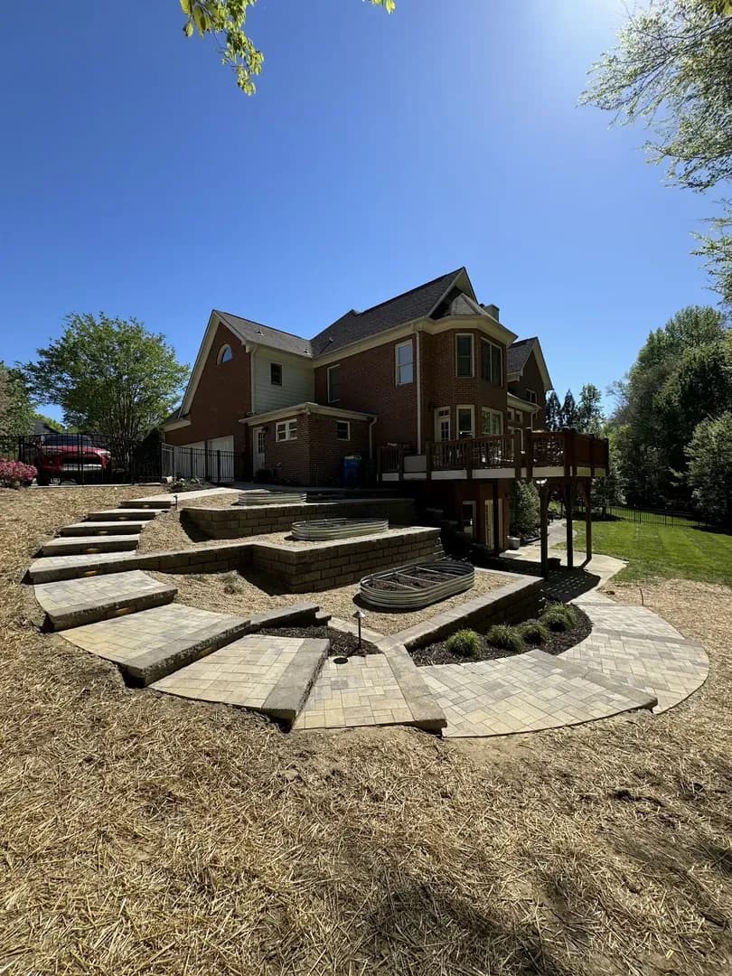 Terraced Paver Patio & Fire Pit by Alex's Lawnscape in Charlotte NC — Multi-level terraced paver patio with retaining wall steps, fire pit area, and fresh straw seeding at a large brick home