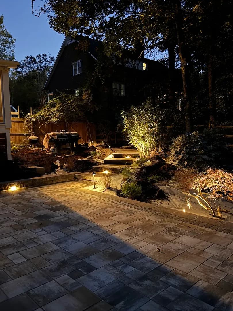 Nighttime Patio & Landscape Lighting by Alex's Lawnscape in Charlotte NC — Paver patio with professional landscape lighting showcasing stone steps, accent-lit plantings, and warm path lights at dusk