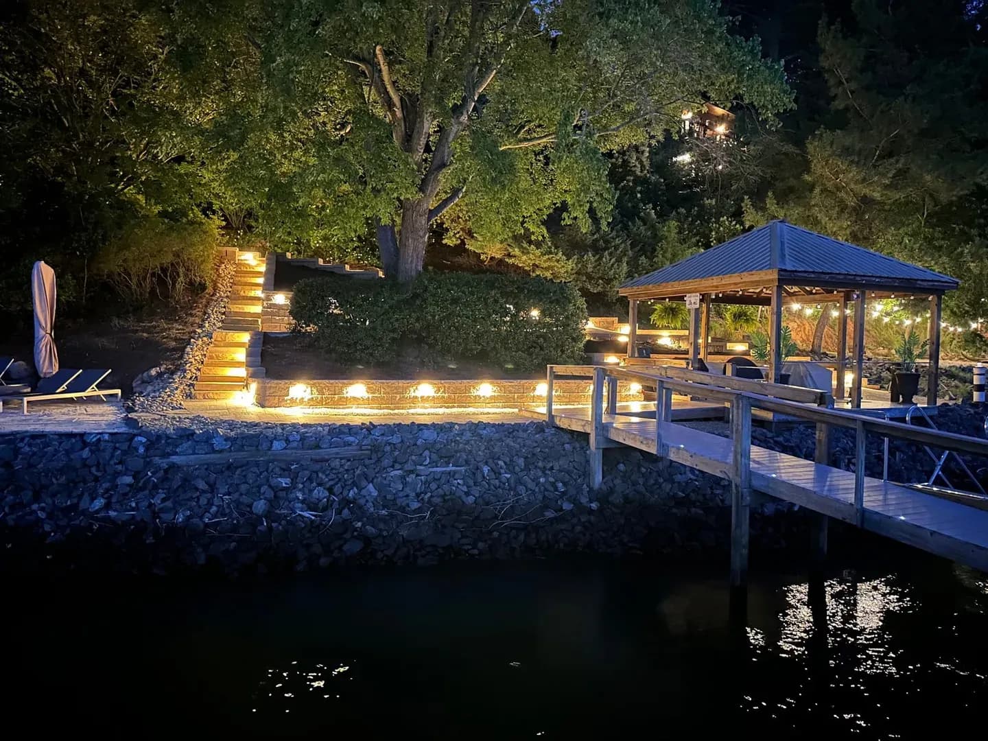 Lakefront Steps with Night Lighting by Alex's Lawnscape in Charlotte NC — Stunning nighttime shot of a lakefront property with illuminated retaining wall steps, dock, and gazebo with string lights