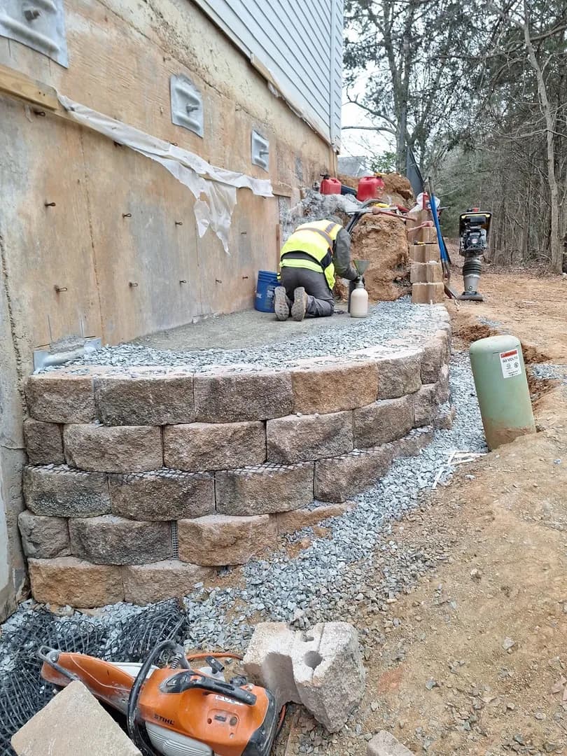 Retaining Wall Build In Progress by Alex's Lawnscape in Charlotte NC — Crew building a natural stone retaining wall with gravel backfill drainage — showing the craftsmanship and heavy equipment that goes into structural stone work